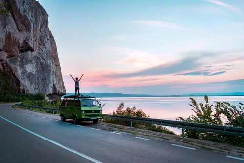 Person standing on top of a green van with arms raised.